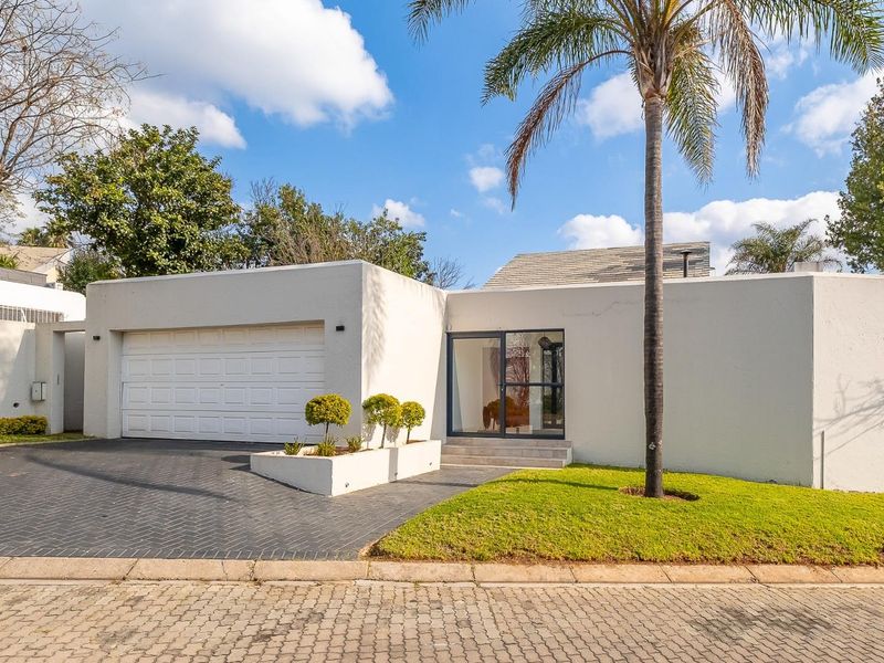 Front elevation of a modern townhouse featuring a double garage, paved driveway, and a well-maintained front lawn with established palm tree.