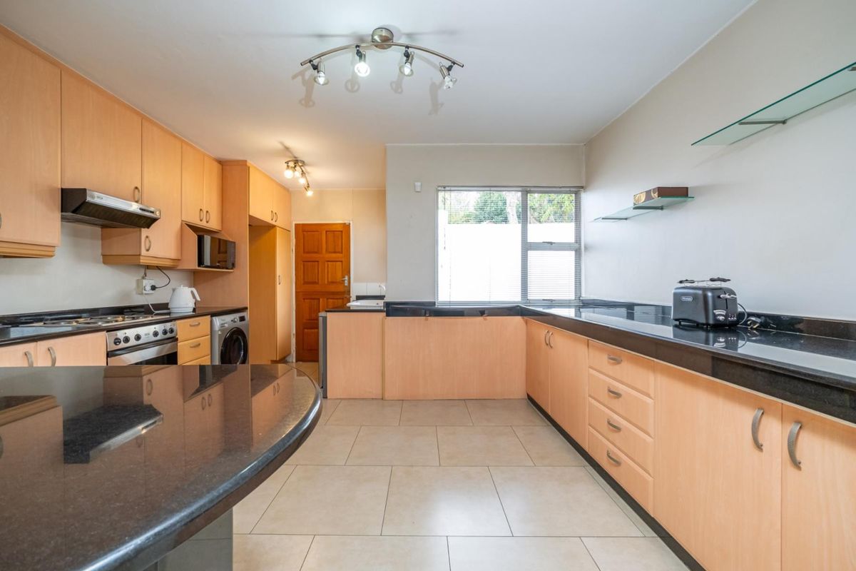 A functional kitchen featuring light wood-tone cabinetry, contrasting black granite countertops, tiled flooring, and integrated appliances, offering a practical layout for daily use.