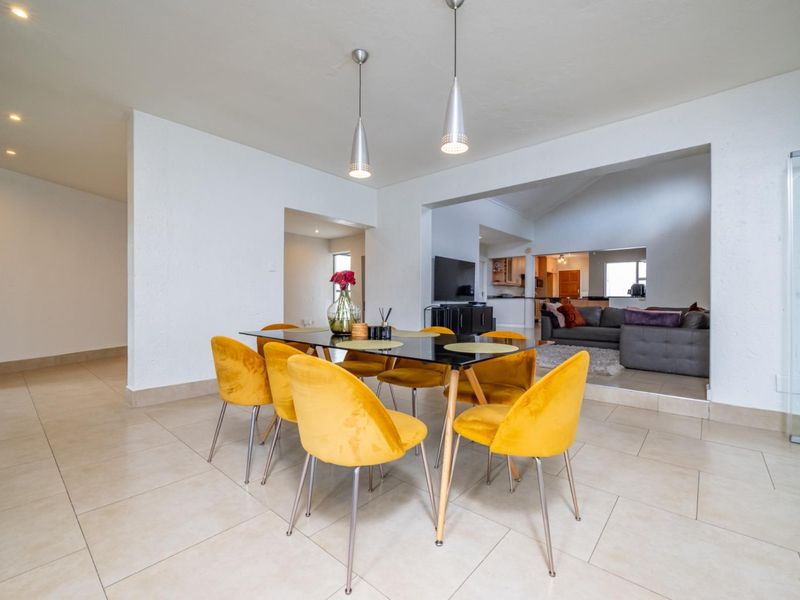An open-plan dining and living area featuring neutral tiled flooring, modern pendant lighting, and a spacious layout connecting to the kitchen.