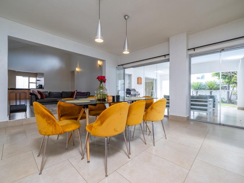 Spacious open-plan dining area featuring large format floor tiles, modern pendant lighting, and seamless access to the outdoor patio through sliding glass doors.