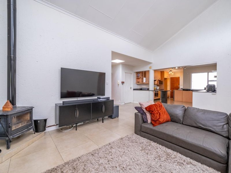 Spacious open-plan living area featuring a vaulted ceiling, tiled floors, and a freestanding fireplace, seamlessly flowing into a functional kitchen space.