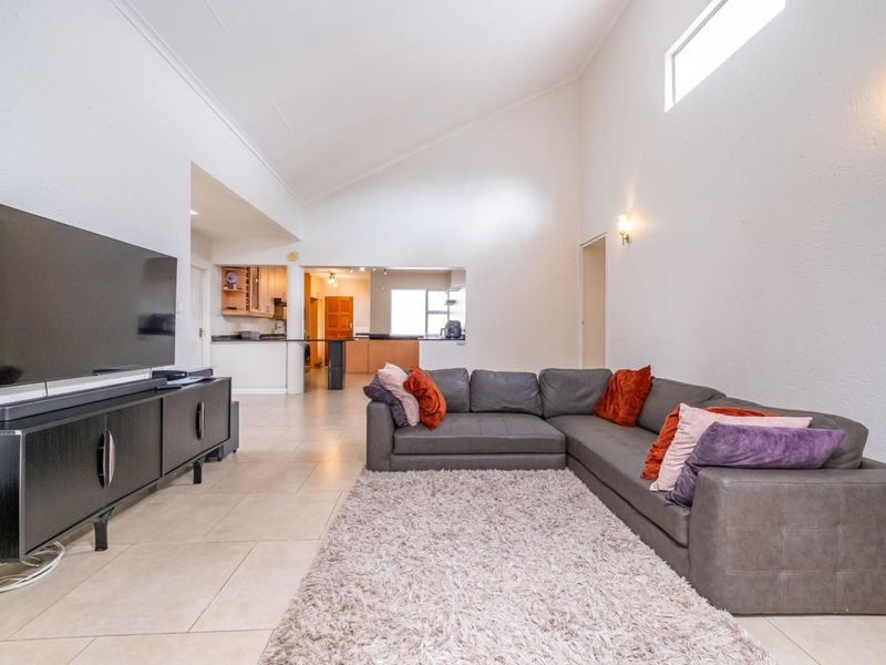 Spacious open-plan living area featuring vaulted ceilings, tiled flooring, and a seamless transition to the kitchen with a breakfast bar.