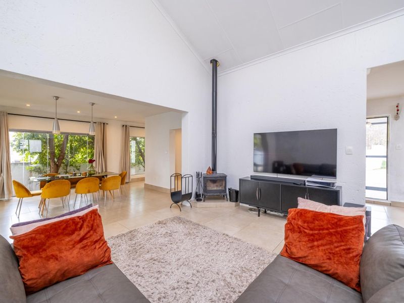 Spacious open-plan living and dining area featuring high vaulted ceilings, tiled floors, and a central freestanding fireplace with direct access to the outdoors.