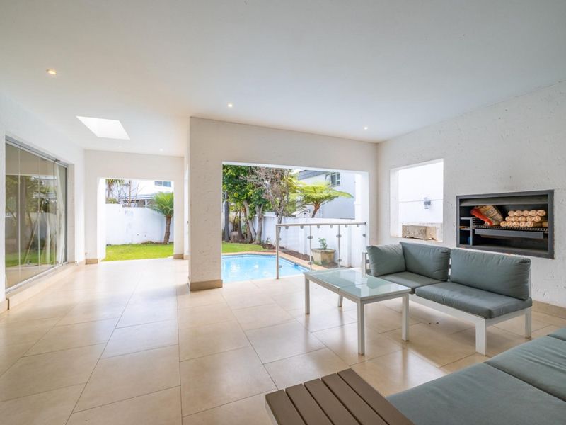 Spacious covered patio featuring tiled flooring, a built-in braai, and seamless flow to the garden and pool area through large glass openings.