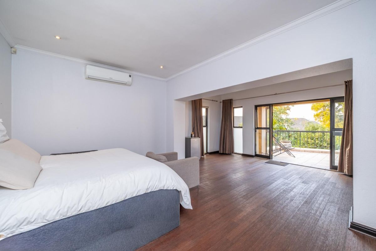 Spacious bedroom featuring dark wood-look flooring, recessed lighting, a wall-mounted air conditioning unit, and direct access to a private balcony.