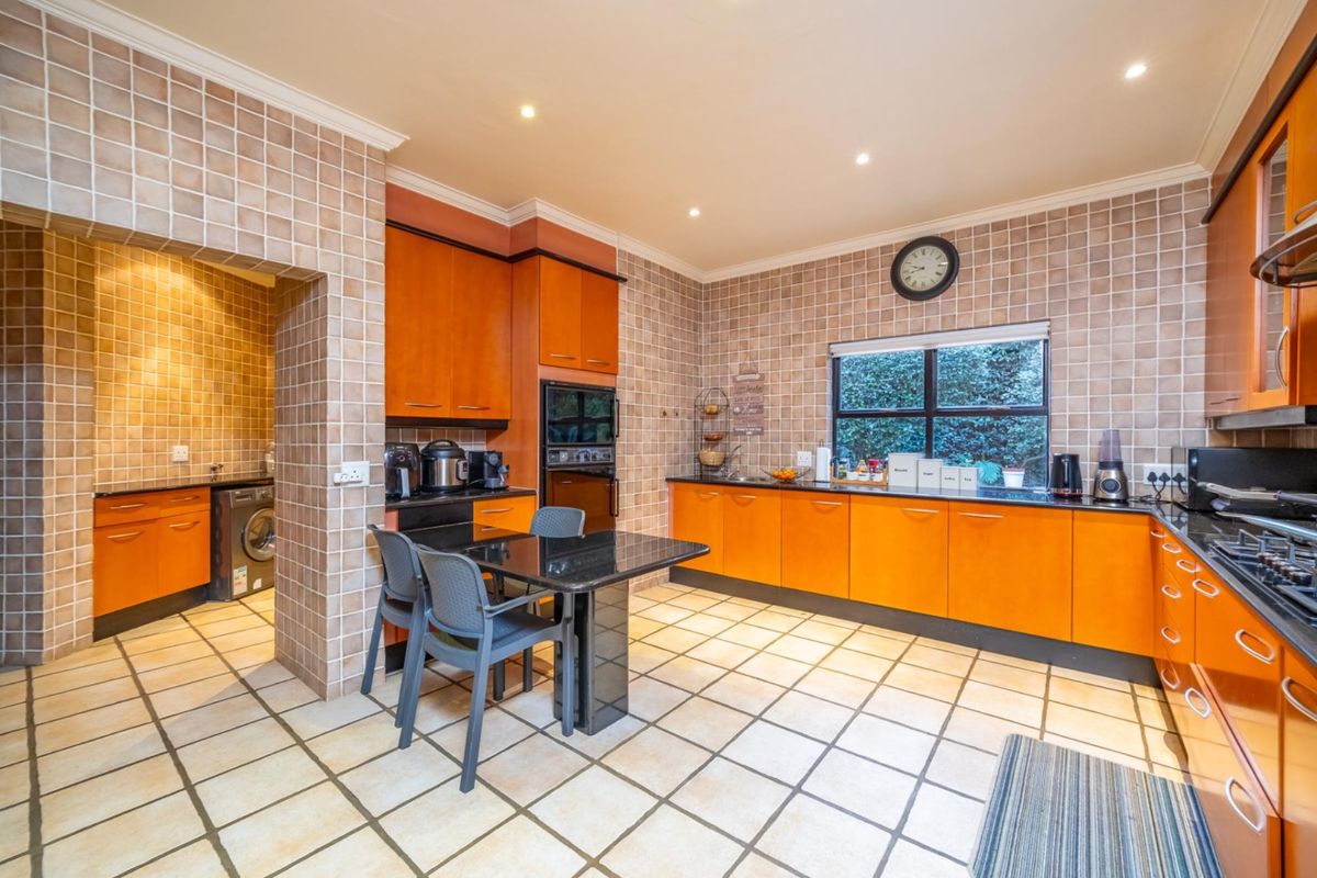 Spacious kitchen featuring orange cabinetry, dark granite countertops, tiled walls and flooring, and an integrated scullery area for laundry appliances.