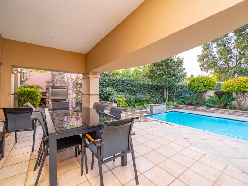 Covered patio area featuring a built-in stone fireplace, tiled flooring, and direct access to a swimming pool and landscaped garden.