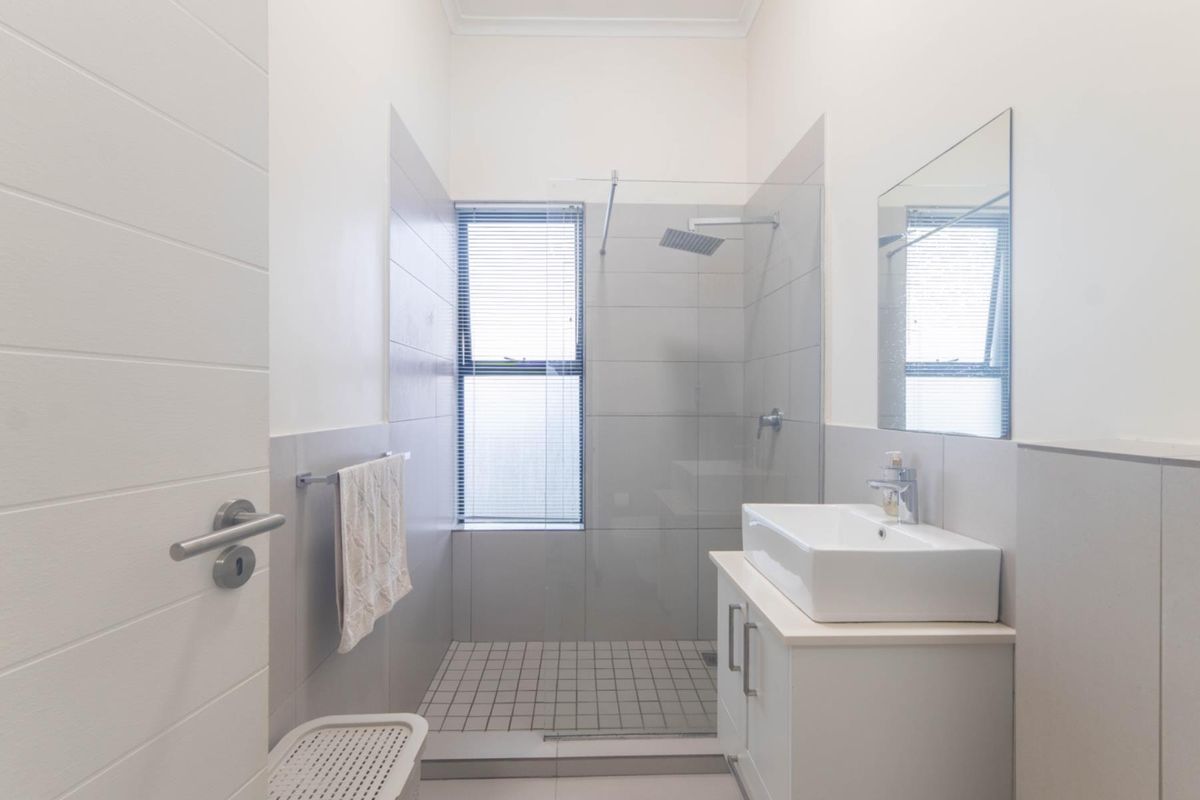 Modern bathroom featuring a walk-in shower with glass screen, contemporary vanity with basin, and neutral wall tiling.