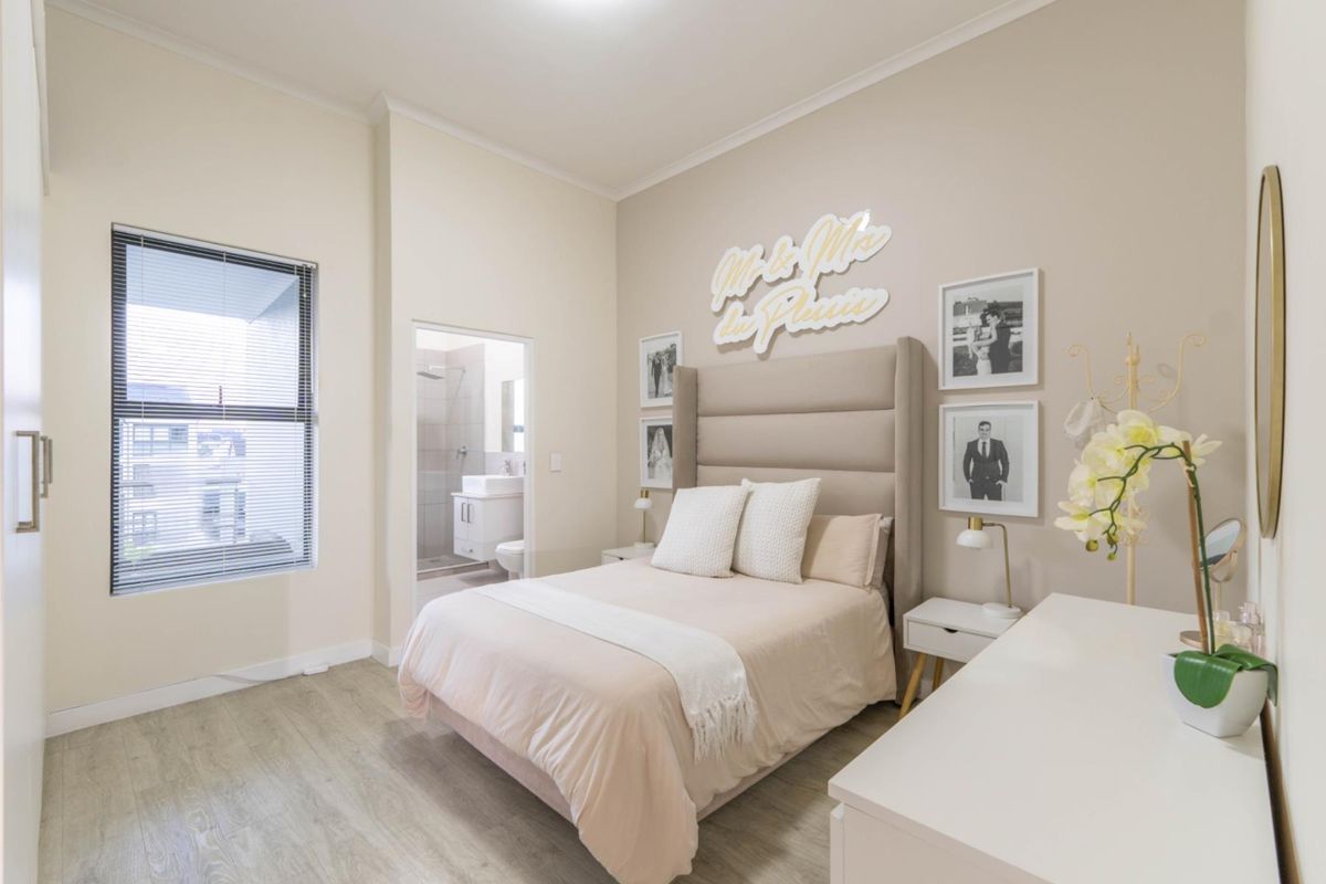 A well-maintained bedroom featuring light wood-look flooring, neutral walls, and an en-suite bathroom with modern fixtures.