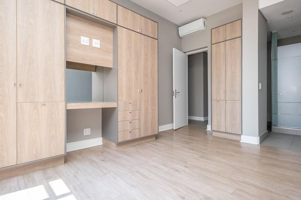 A modern, well-maintained bedroom featuring extensive built-in cabinetry, a dedicated vanity area, laminate flooring, and an integrated split-system air conditioner.