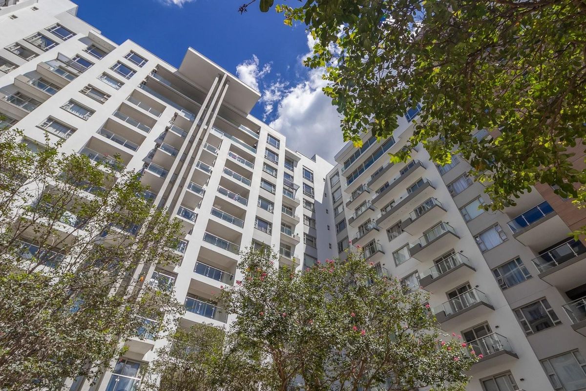 Low-angle view of a modern multi-story apartment building featuring white facade finishes and glass-railed balconies.