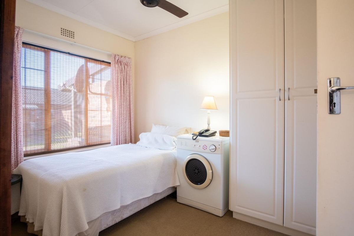 A bedroom featuring built-in cupboards, a ceiling fan, and a window with blinds, currently utilized with a laundry appliance.
