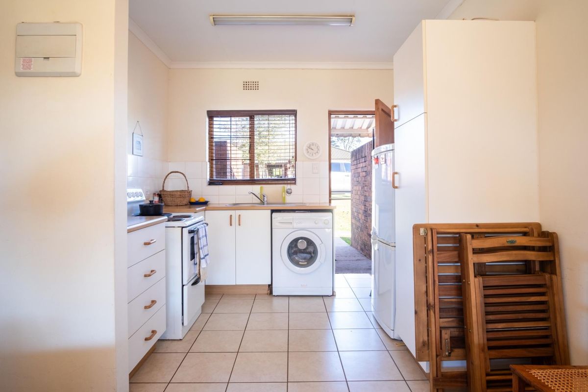 A functional kitchen featuring white cabinetry, tiled flooring, a built-in stove, and a dedicated space for laundry appliances with direct access to the exterior.