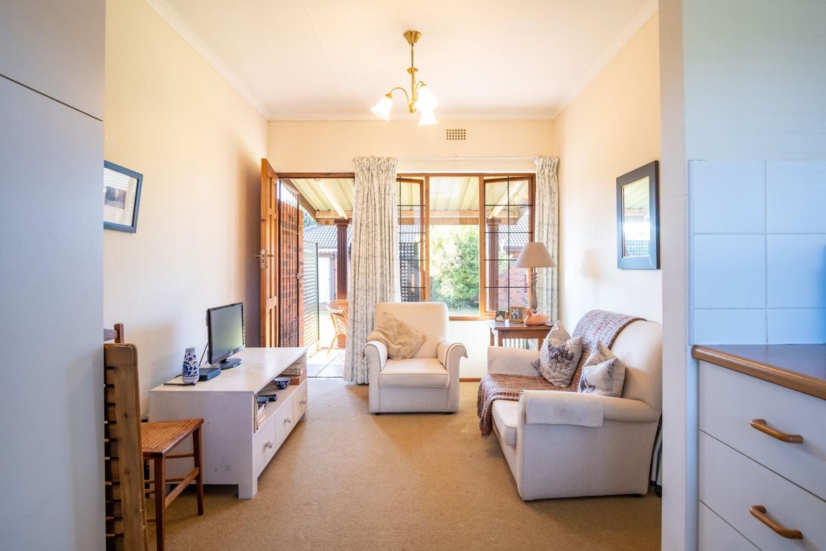 A cozy living room featuring carpeted flooring, a ceiling light fixture, and direct access to an outdoor patio area through a wooden door.