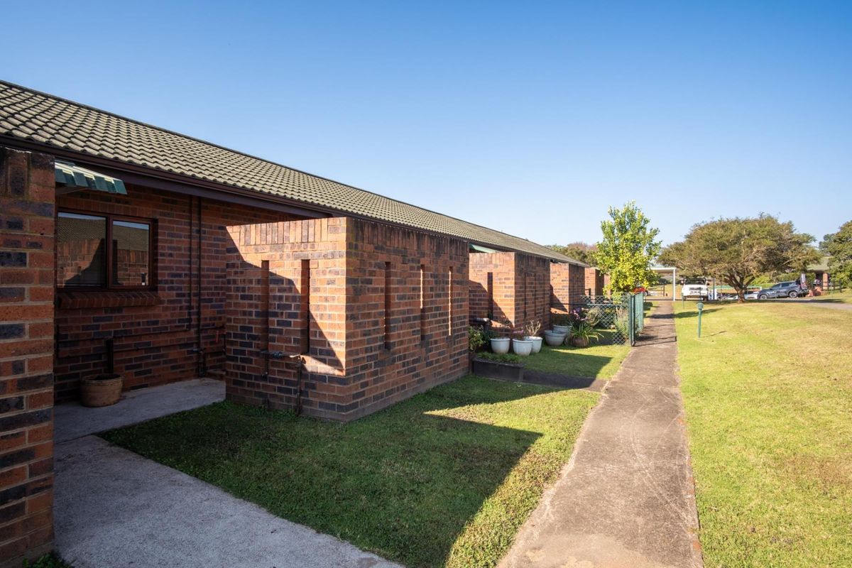 Exterior view of a brick residential building featuring a tiled roof, concrete walkway, and private brick-enclosed outdoor utility or patio areas.