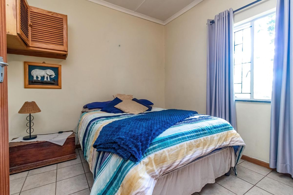 A functional bedroom featuring tiled flooring, a window with curtaining, and a wall-mounted wooden storage cabinet.