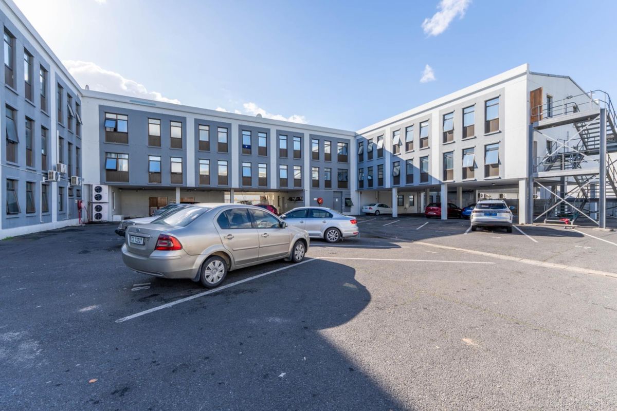 Exterior view of the apartment complex featuring a paved parking courtyard and multi-story building facade with numerous windows.