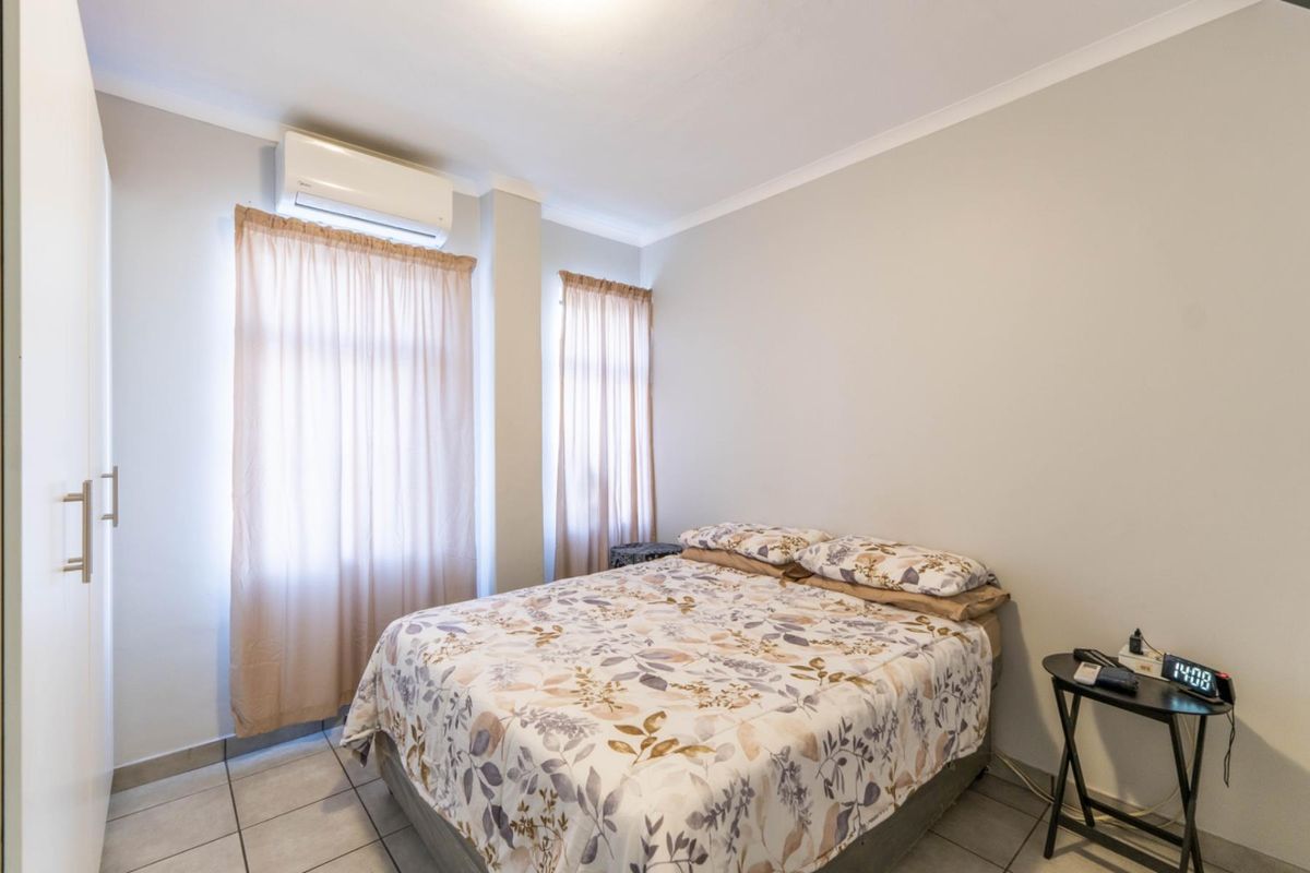A functional bedroom featuring tiled flooring, built-in cupboards, and a wall-mounted air conditioning unit.
