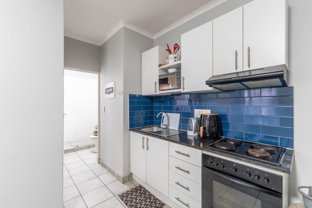 Compact kitchen featuring white cabinetry, dark granite countertops, blue subway tile backsplash, and a built-in oven with extractor fan.