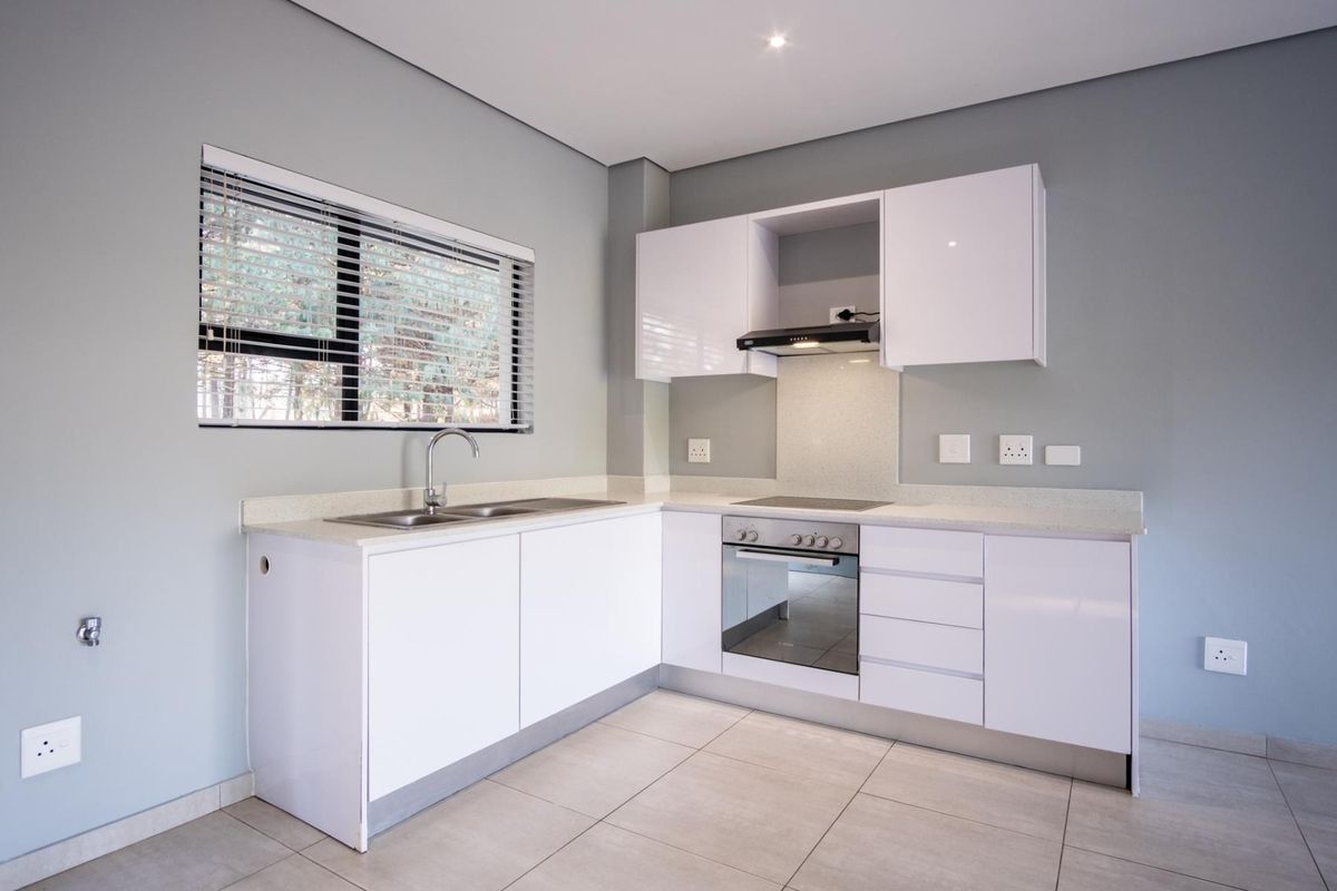Modern kitchen featuring white high-gloss cabinetry, stone countertops, integrated oven, hob, and extractor fan, complemented by neutral tiled flooring and a large window.