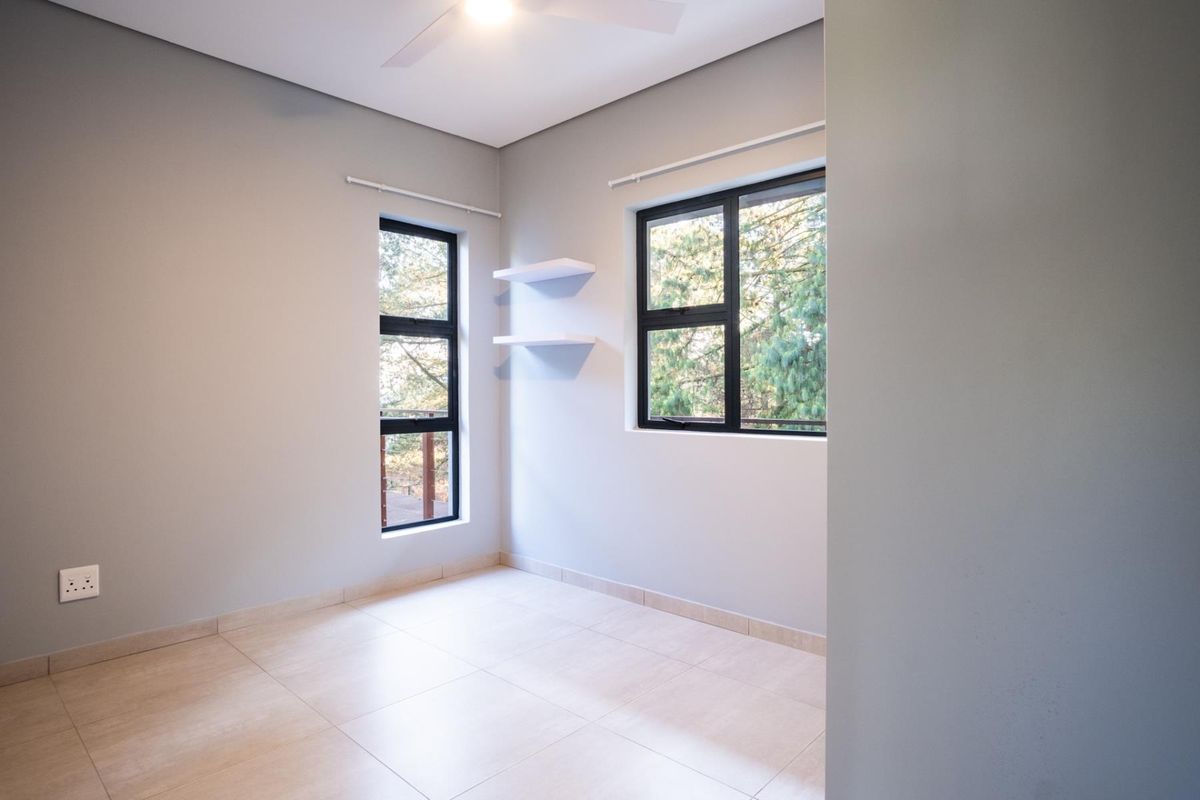 A bright, empty bedroom featuring neutral tiled flooring, modern black-framed windows, and built-in wall shelving.
