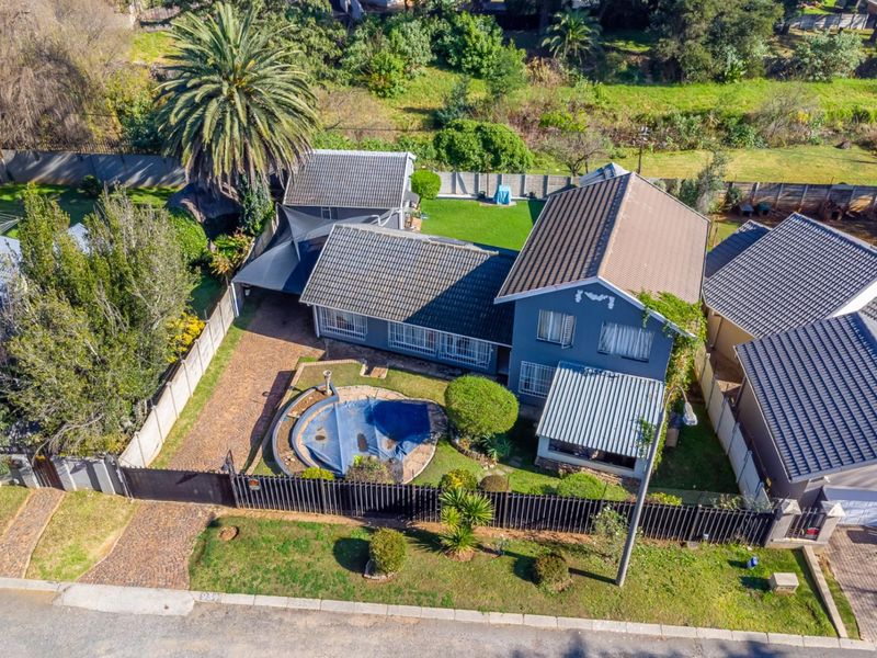 Aerial view of a residential property featuring a tiled roof house, swimming pool, paved driveway, and established garden area.