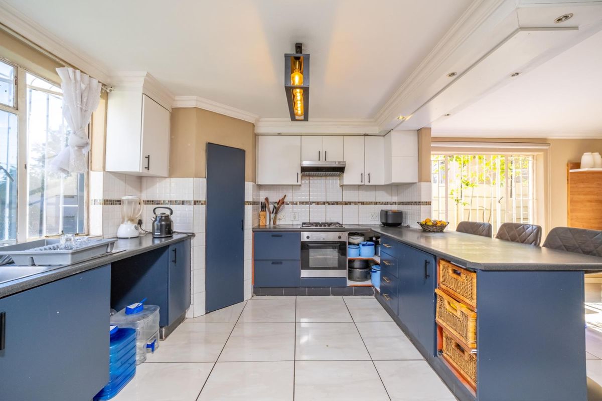 A functional kitchen featuring dark blue lower cabinetry, white upper cabinets, tiled flooring, and integrated appliances including a gas hob and oven.