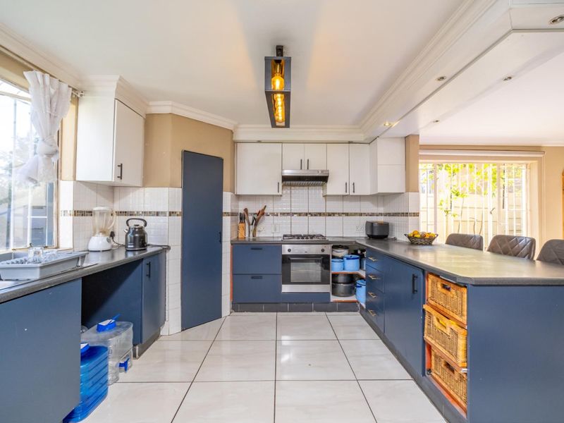 A functional kitchen featuring dark blue lower cabinetry, white upper cabinets, tiled flooring, and integrated appliances including a gas hob and oven.