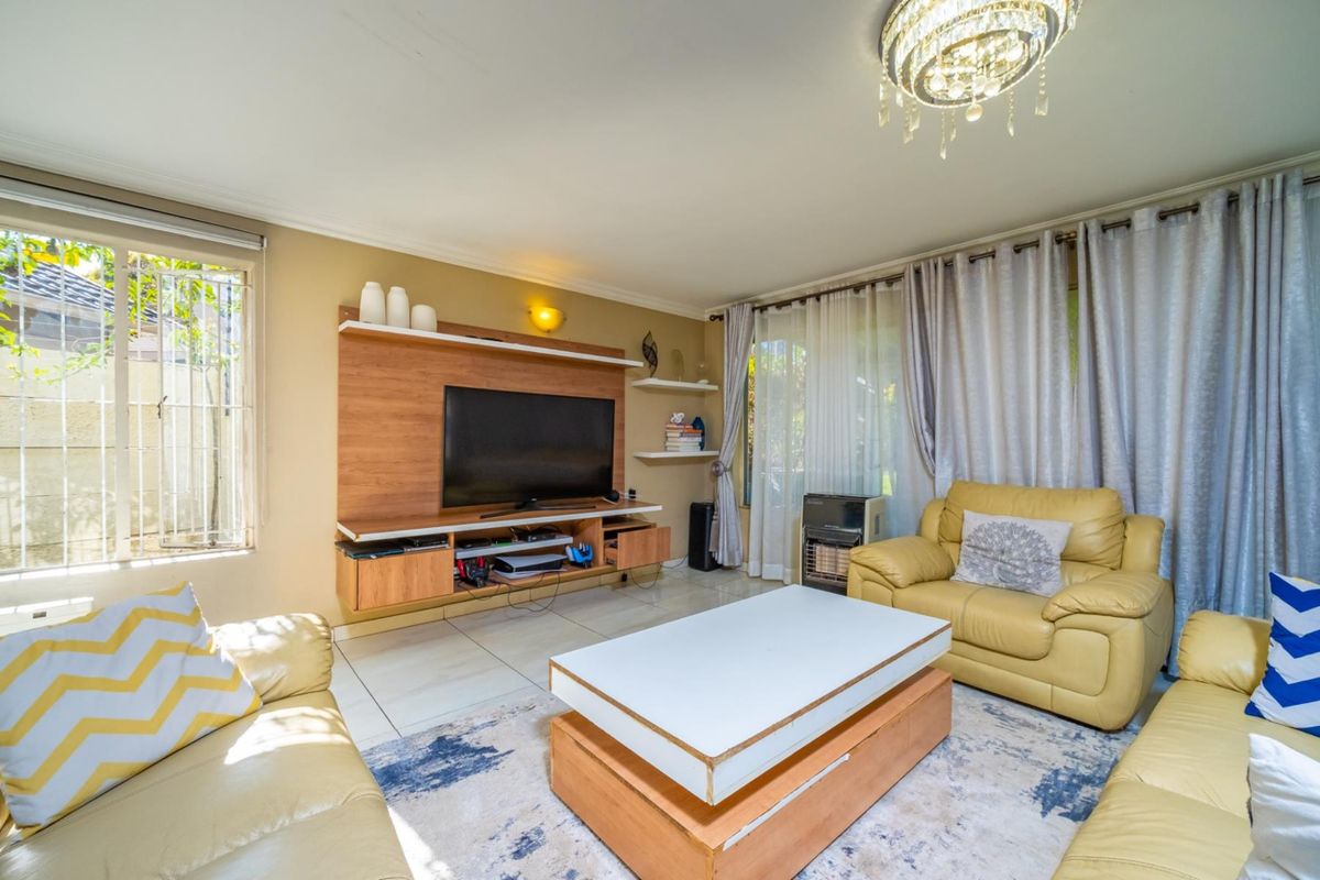 A comfortable living room featuring a built-in media unit, tiled flooring, and a decorative crystal chandelier, with access to the garden through sliding doors.