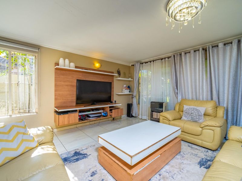 A comfortable living room featuring a built-in media unit, tiled flooring, and a decorative crystal chandelier, with access to the garden through sliding doors.