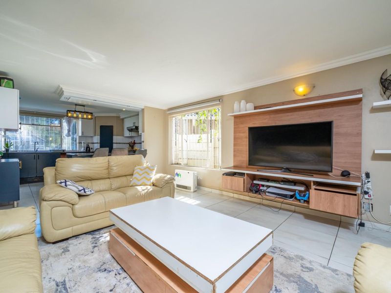 Open-plan living area featuring tiled floors, a built-in media unit, and a connected kitchen space with cabinetry and island.