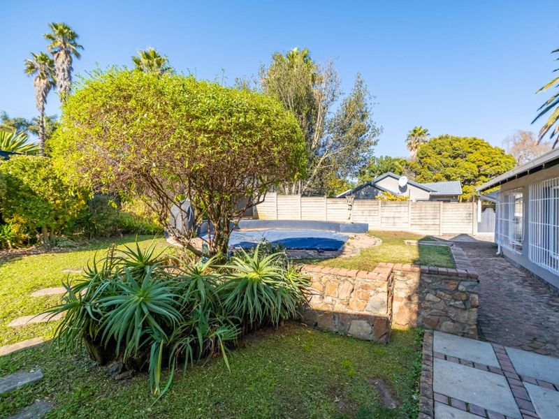 A backyard area featuring a swimming pool with a cover, stone retaining wall, paved pathways, and established garden landscaping.