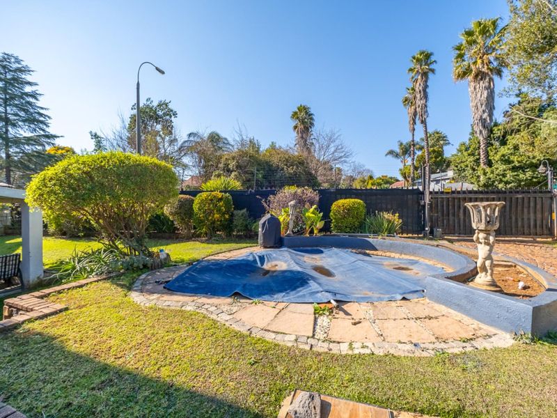 Outdoor pool area featuring a circular swimming pool with a cover, surrounded by stone paving and a landscaped garden with boundary fencing.