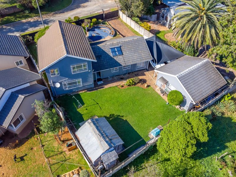 Aerial view of a residential property featuring a main house with a tiled roof, a swimming pool, a garden, and a detached outbuilding.