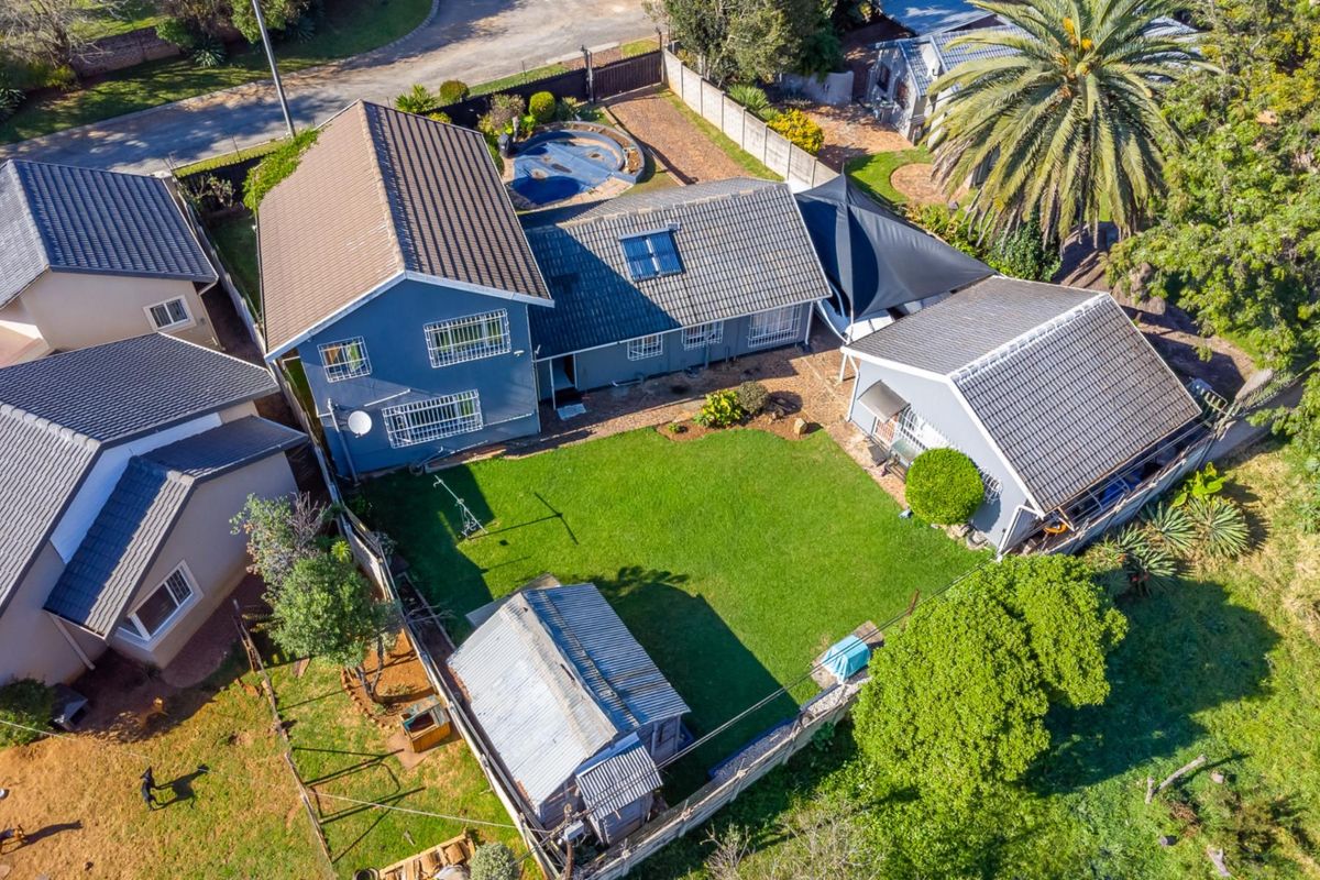 Aerial view of a residential property featuring a main house with a tiled roof, a swimming pool, a garden, and a detached outbuilding.