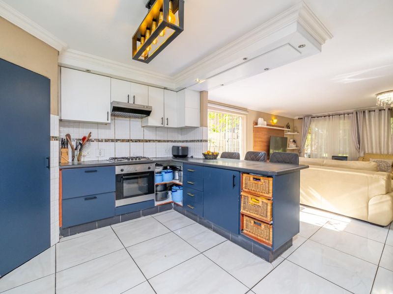 Open-plan kitchen featuring blue and white cabinetry, built-in oven, gas hob, and a breakfast bar, seamlessly flowing into the adjacent living area.