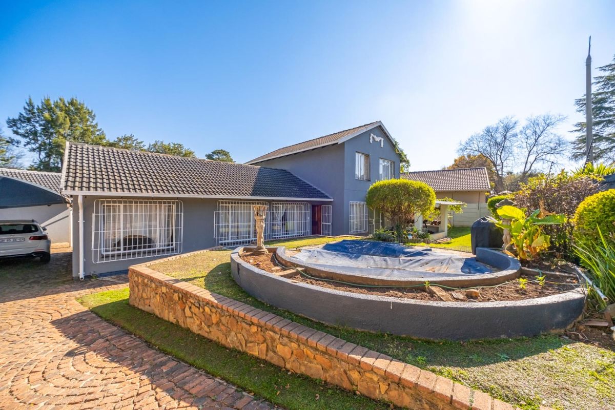 Rear exterior view of the house featuring a paved driveway, stone retaining wall, and a swimming pool with a cover.