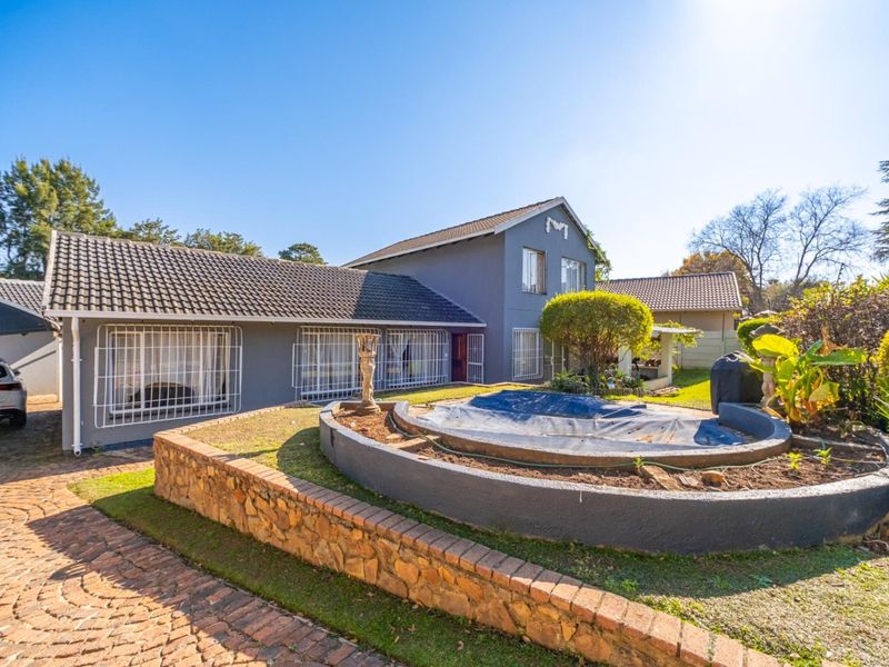 Rear exterior view of the house featuring a paved driveway, stone retaining wall, and a swimming pool with a cover.