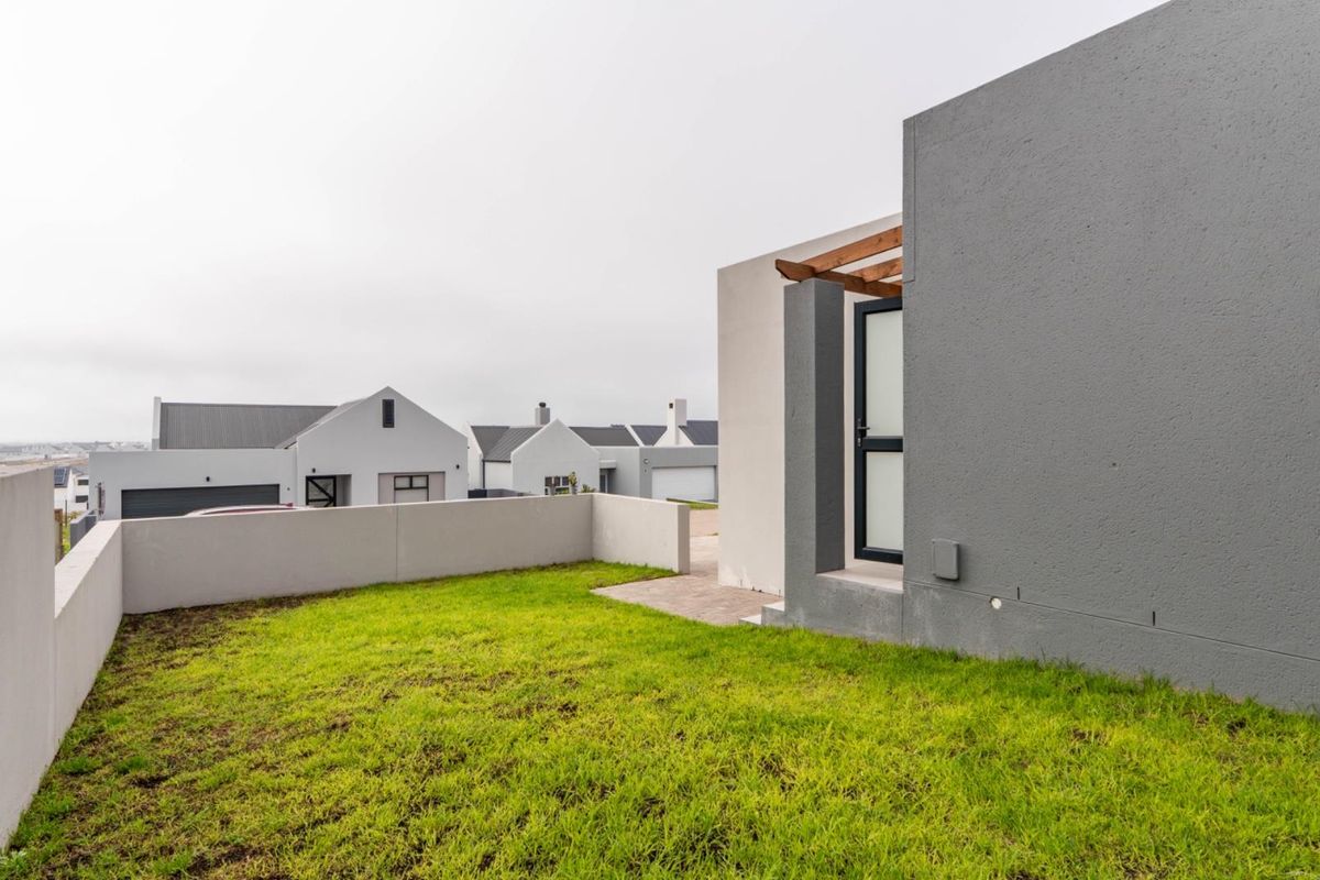 A view of the rear garden area featuring a small paved patio section, a lawn, and a modern exterior wall with a pergola detail.