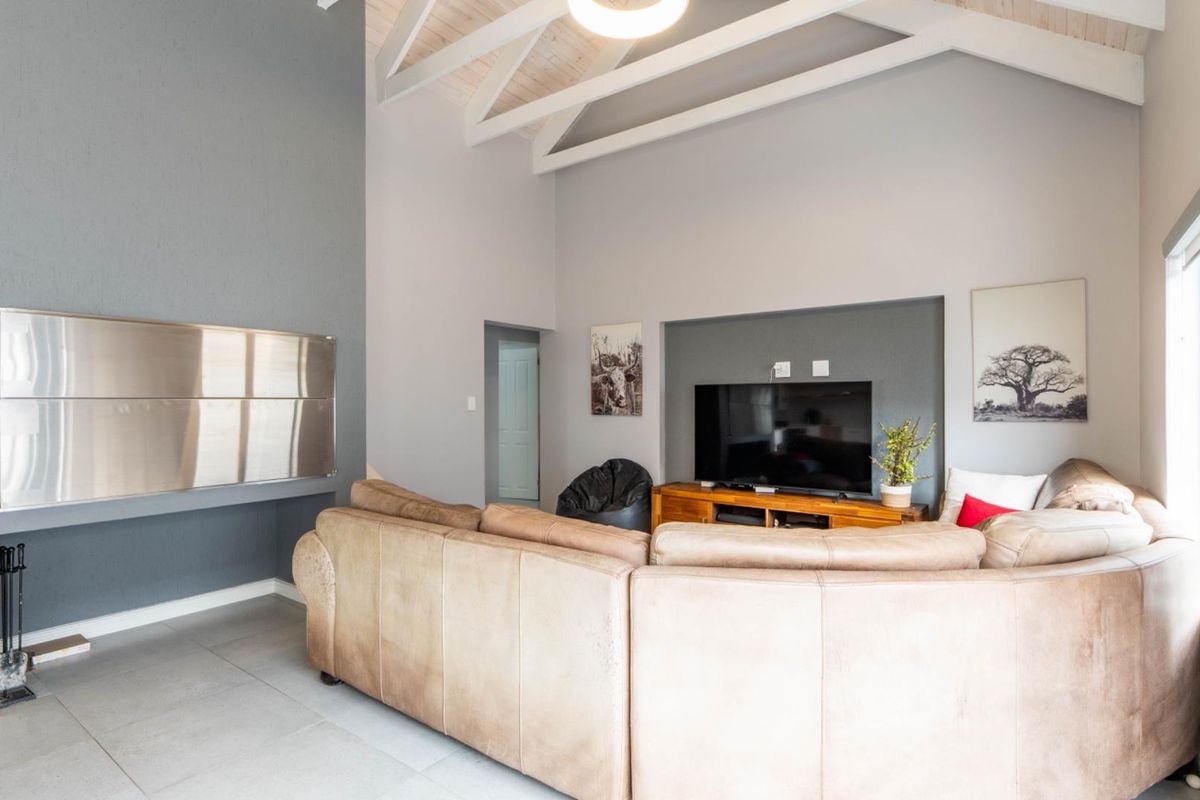 Spacious living room featuring high vaulted ceilings with exposed beams, tiled flooring, and a built-in stainless steel fireplace.