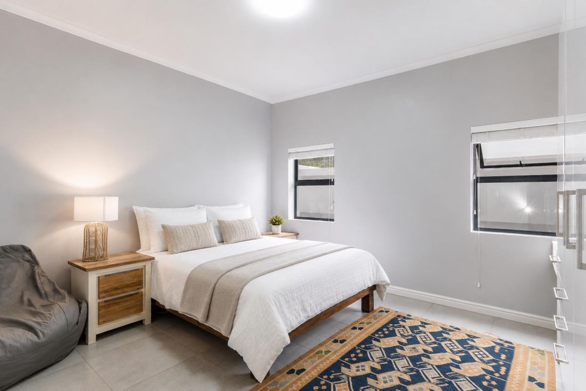 A bright and modern bedroom featuring neutral wall tones, tiled flooring, and built-in wardrobe storage with sleek handles.