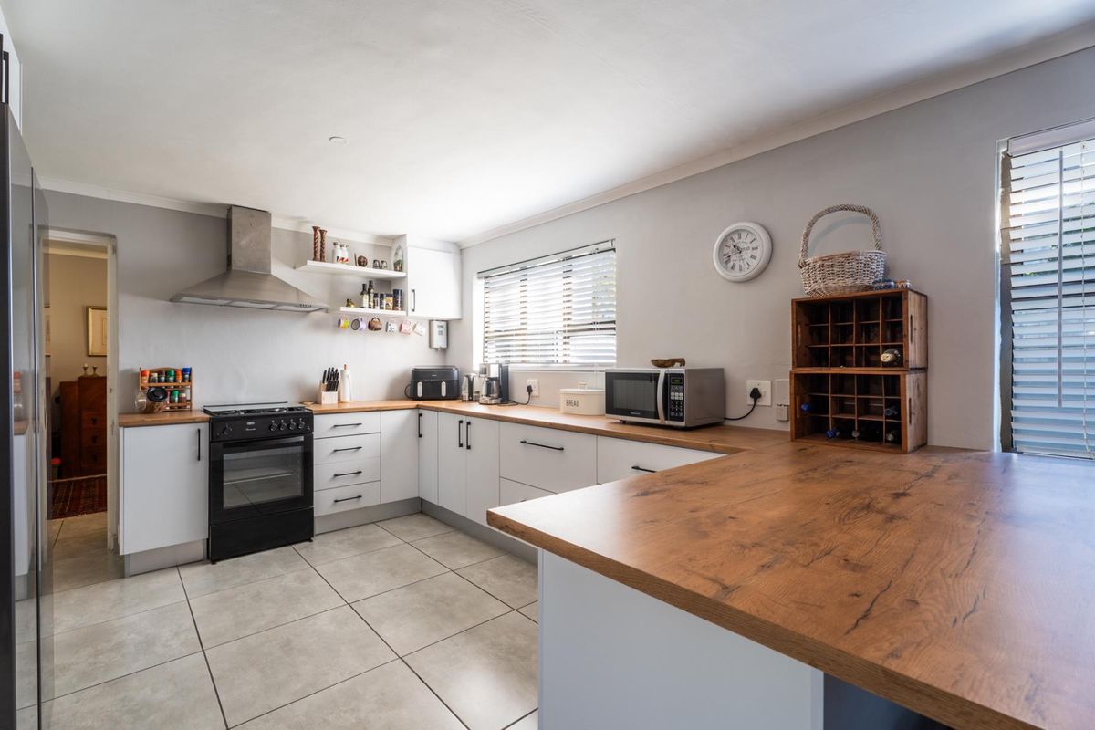 Modern kitchen featuring white cabinetry, warm wooden countertops, stainless steel extractor fan, and tiled flooring with ample natural light.