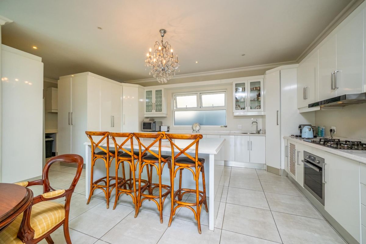 Modern kitchen featuring white cabinetry, a central island with breakfast bar seating, integrated oven, gas hob, and tiled flooring.