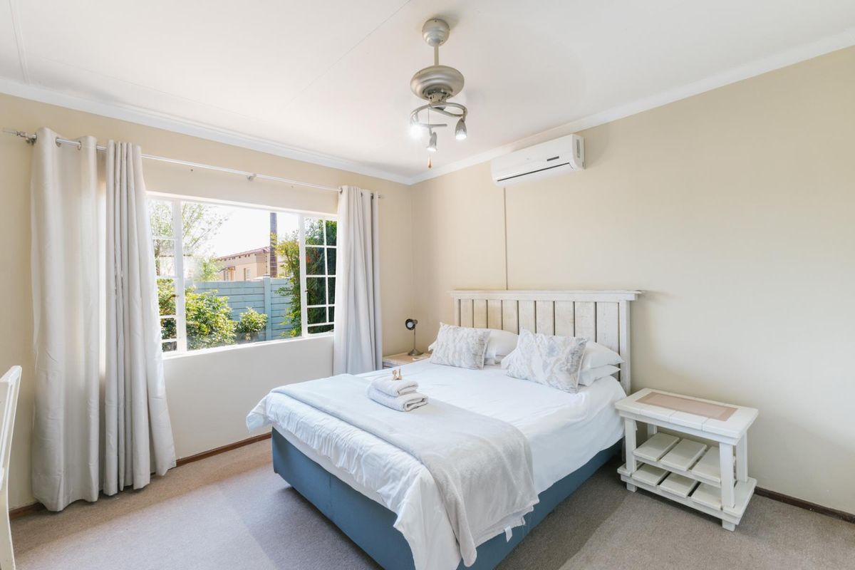 A well-maintained bedroom featuring neutral walls, carpeted flooring, an air conditioning unit, and a ceiling fan with natural light from the window.