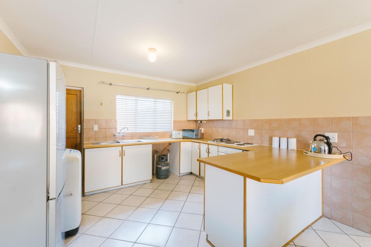 Functional kitchen featuring white cabinetry, laminate countertops, tiled backsplash, gas hob, and tiled flooring with a breakfast nook area.