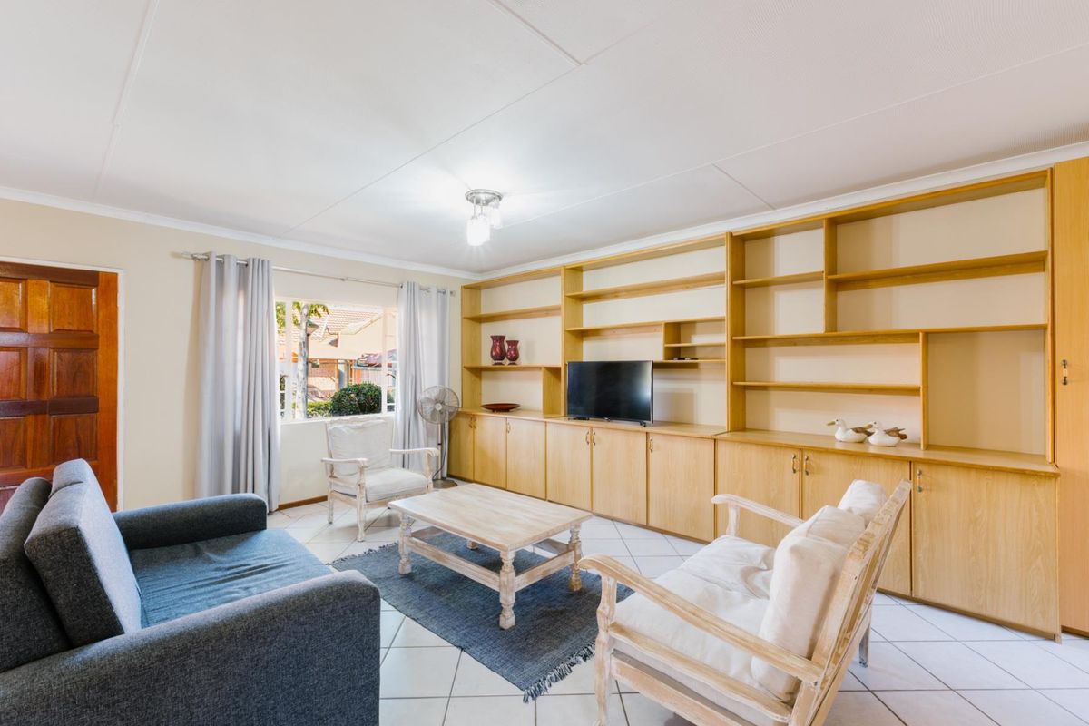 A living room featuring extensive built-in wooden cabinetry and shelving, tiled flooring, and natural light from a window.