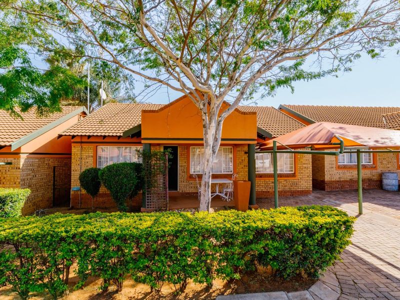 Front elevation of a face brick townhouse featuring a tiled roof, a paved driveway, and a covered carport area.