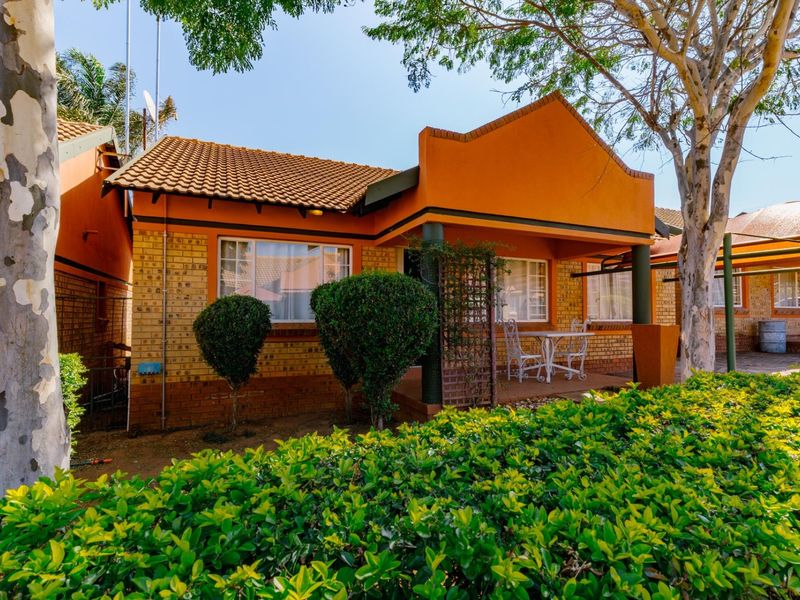 Front view of a townhouse featuring a covered patio, facebrick exterior, and terracotta roof tiles, set within a landscaped residential complex.