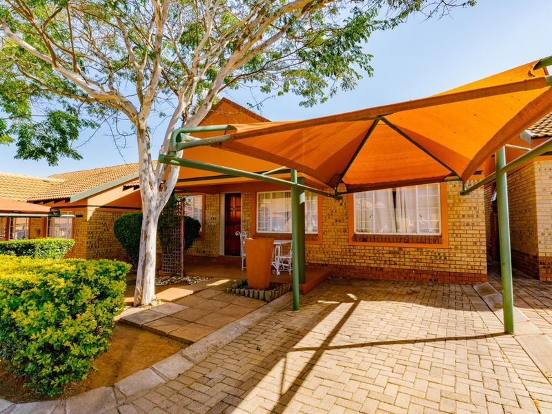 Front exterior view of a face brick townhouse featuring a paved driveway and a large orange shade sail structure.