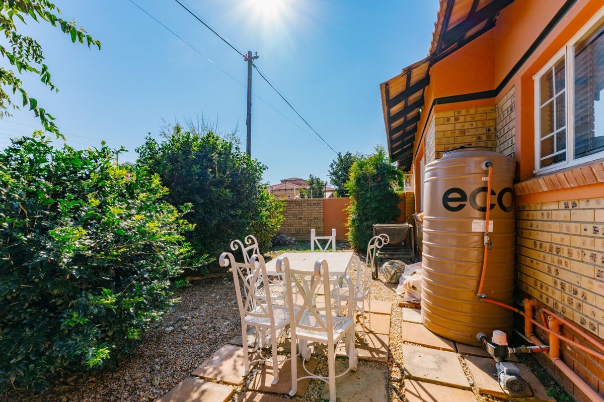 A rear garden area featuring a paved patio, brick boundary wall, and a plumbed water storage tank with an external pump.